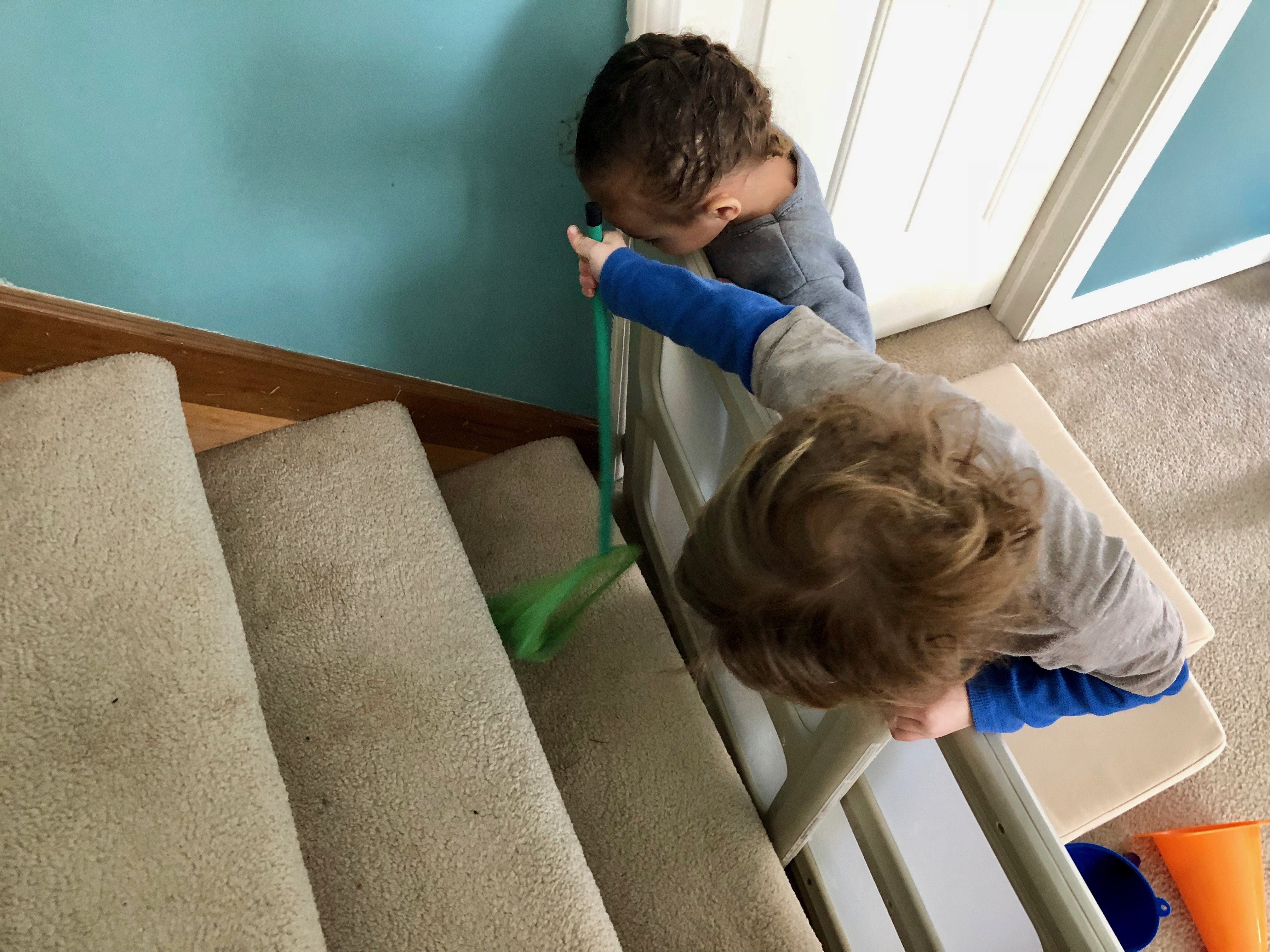 boy using a net to try to reach bell in a small crevice on the stairs
