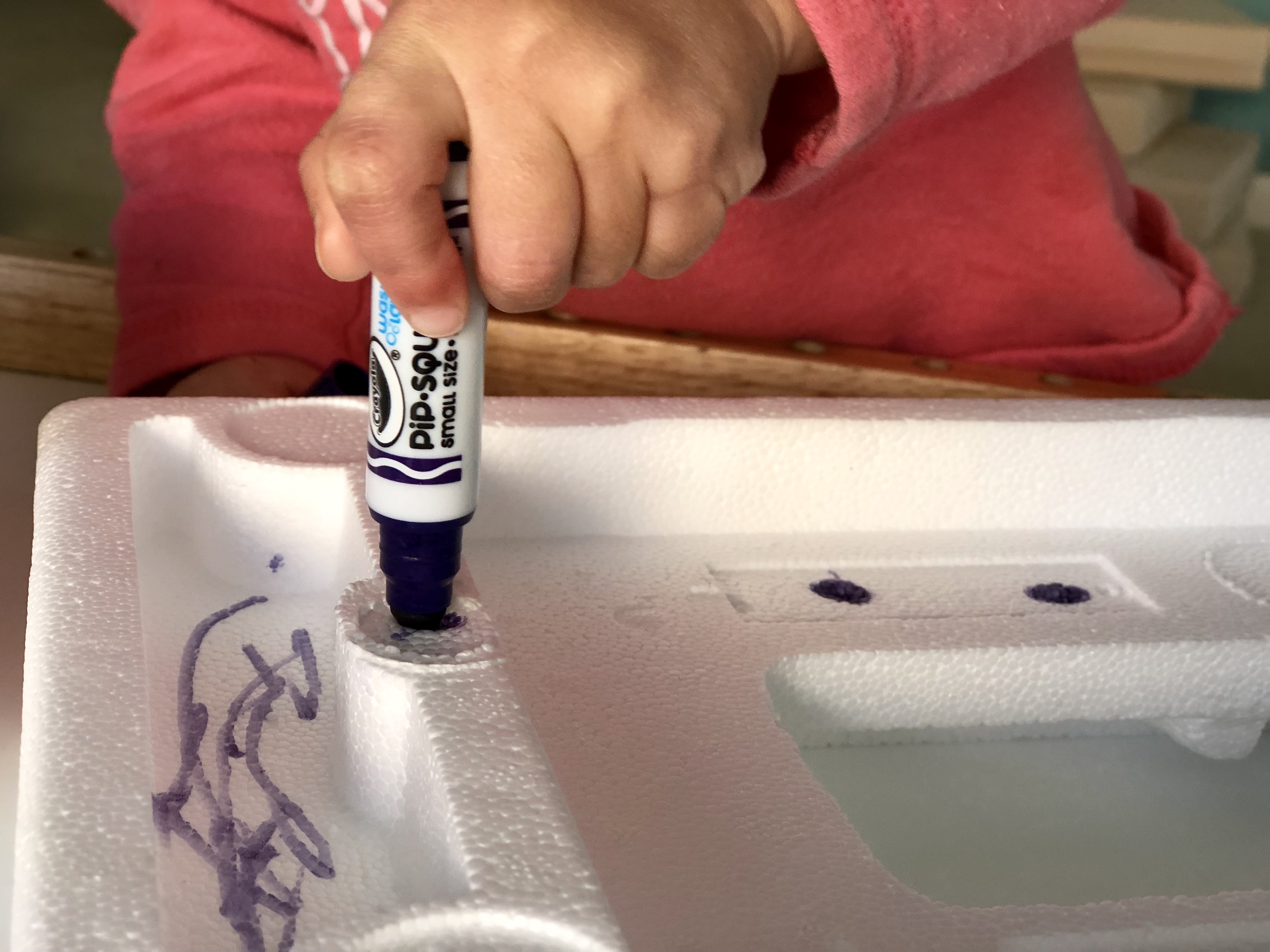 child's hand pushing a marker into a piece of styrofoam