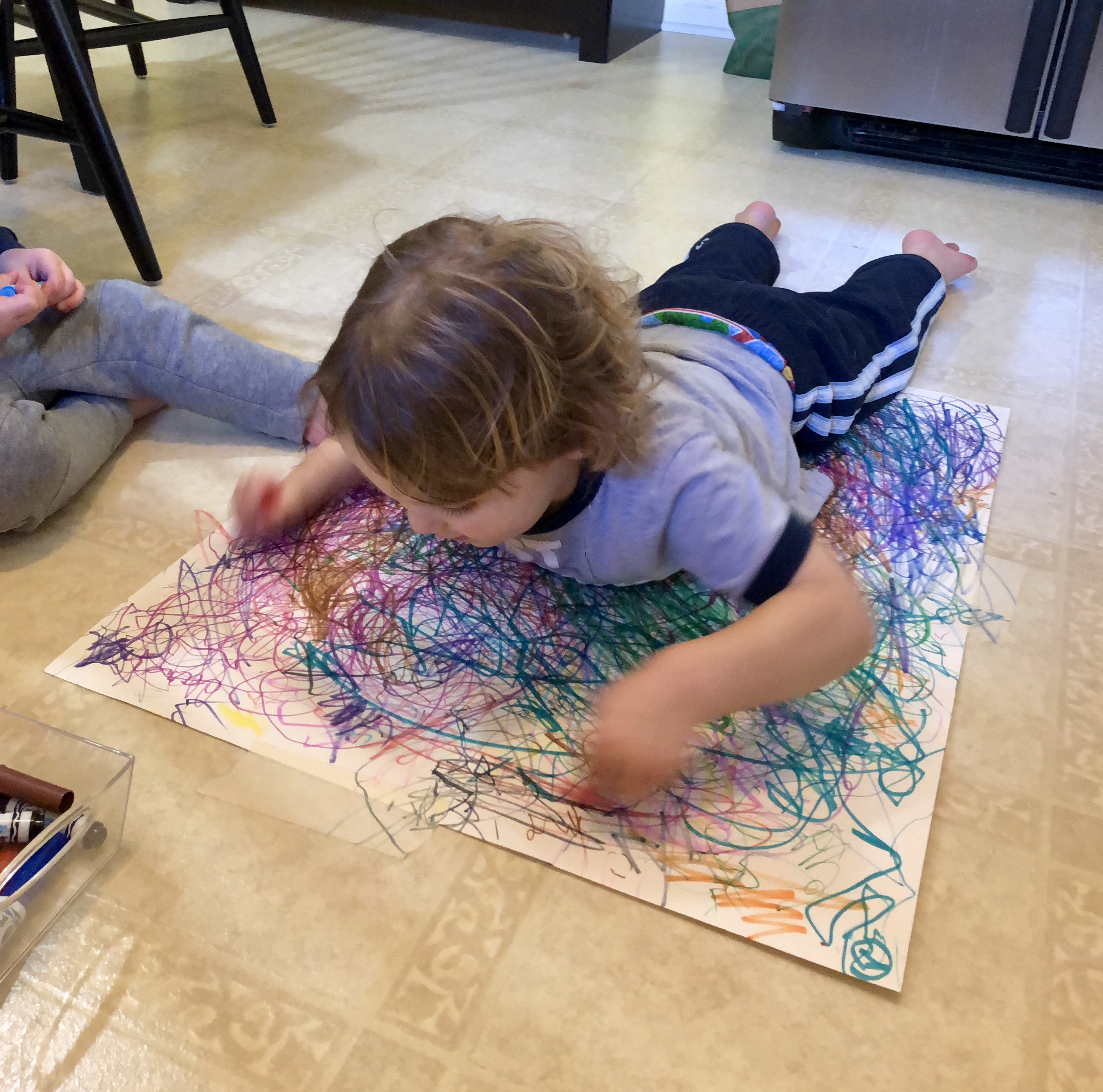 boy laying down on a large sheet of paper and waving the markers in his hands