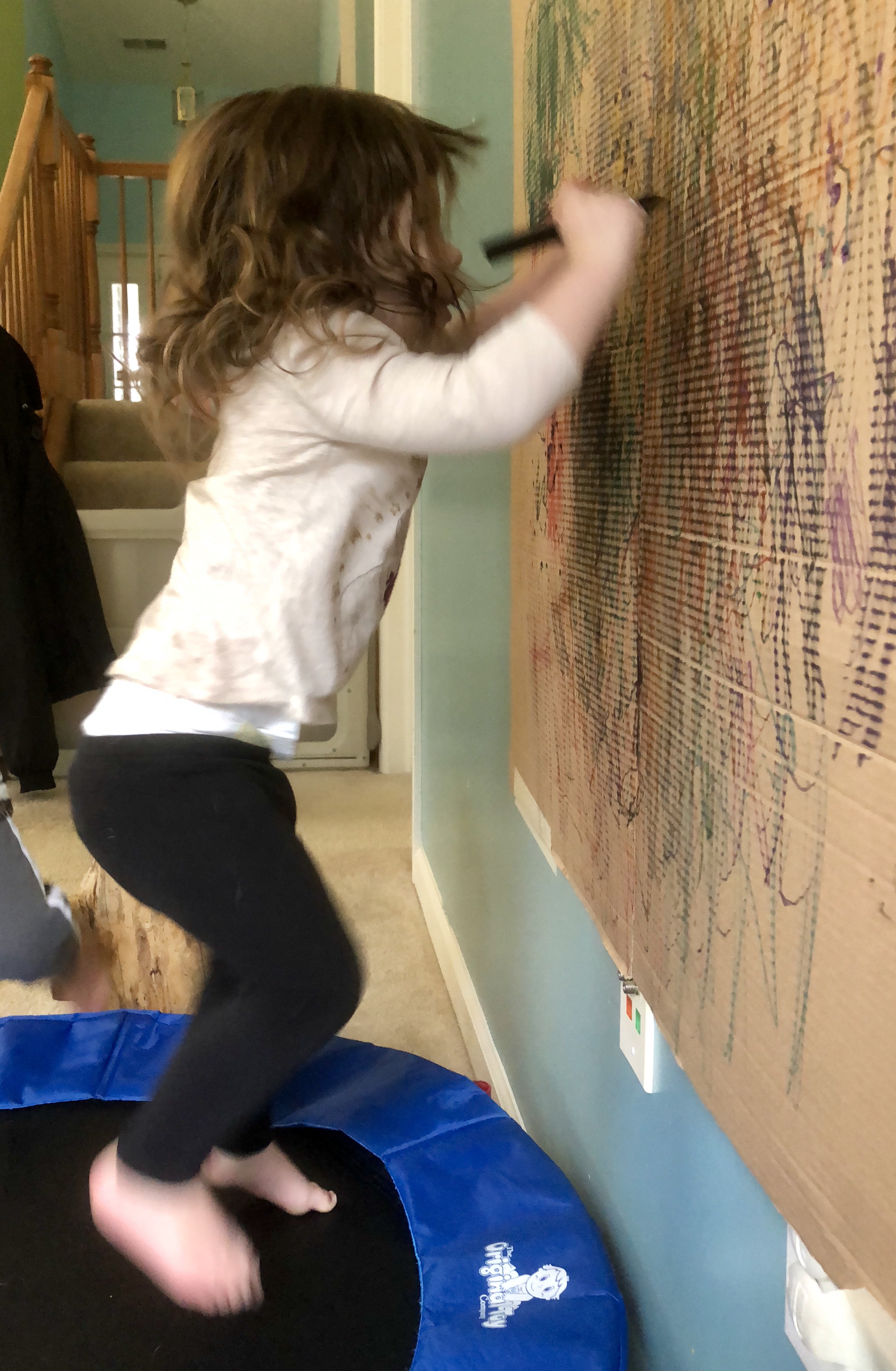 girl jumping on a trampoline and marking on a large piece of cardboard