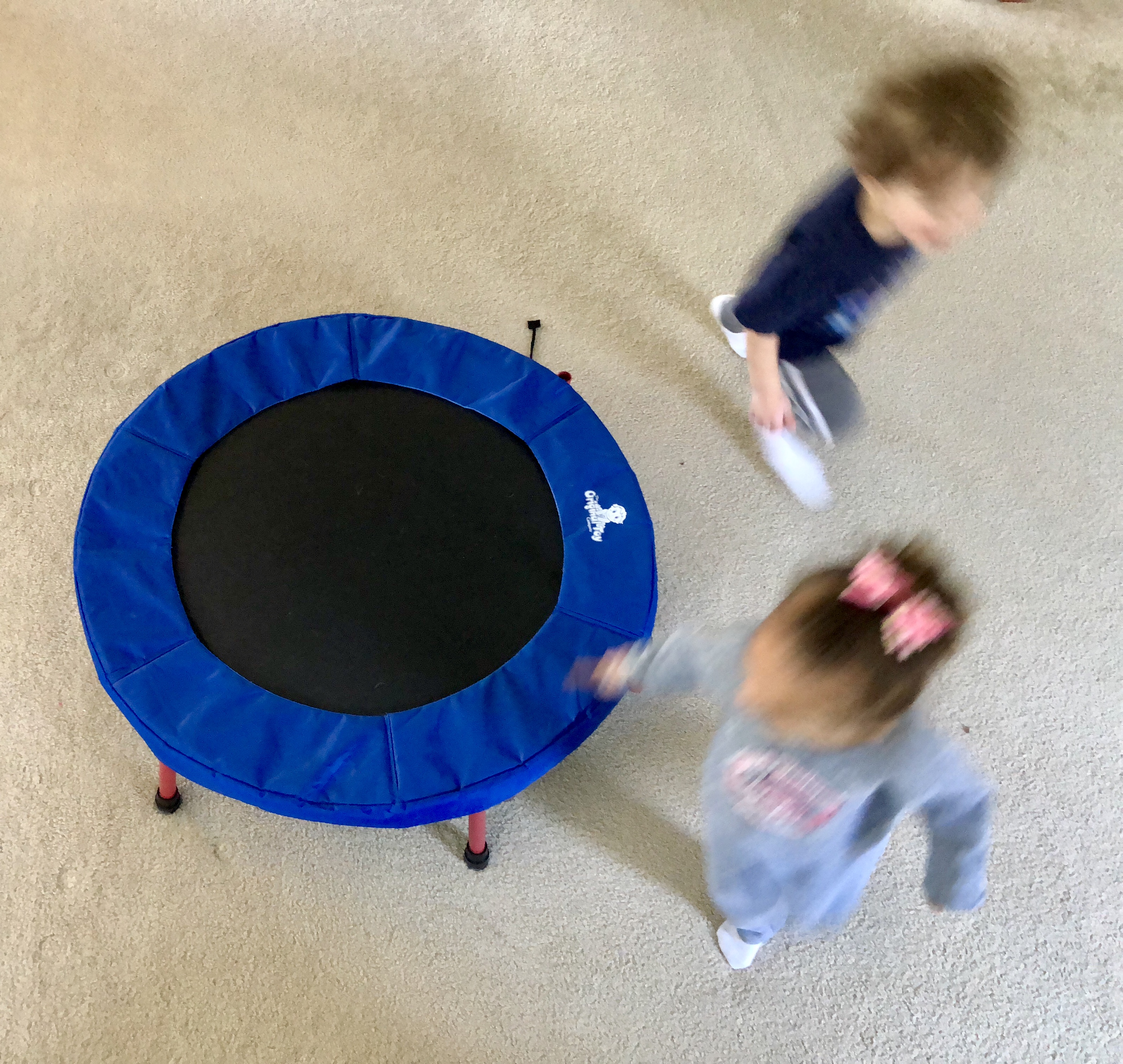 blurry image of 2 children running around a trampoline