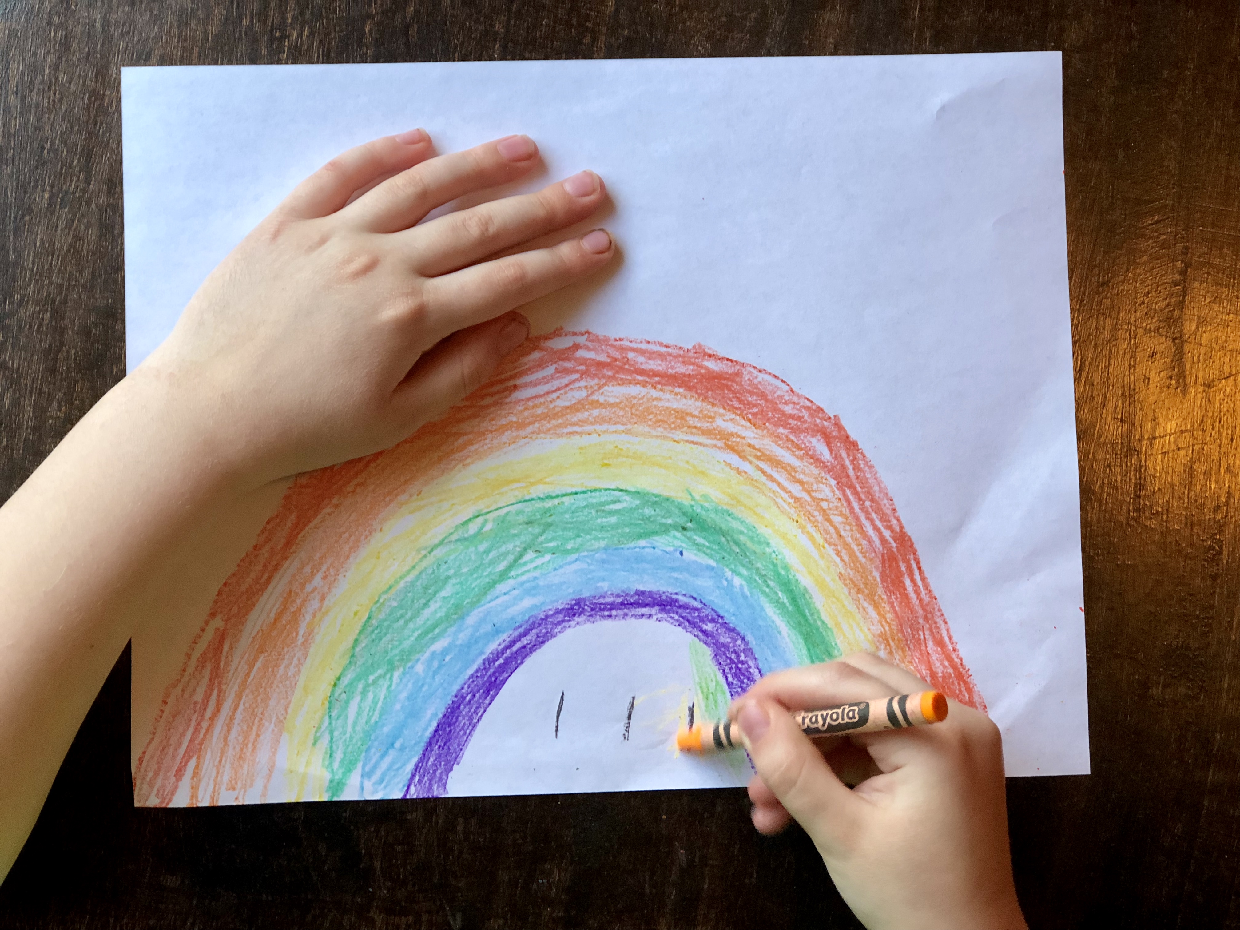 child's hand drawing a rainbow with a crayon