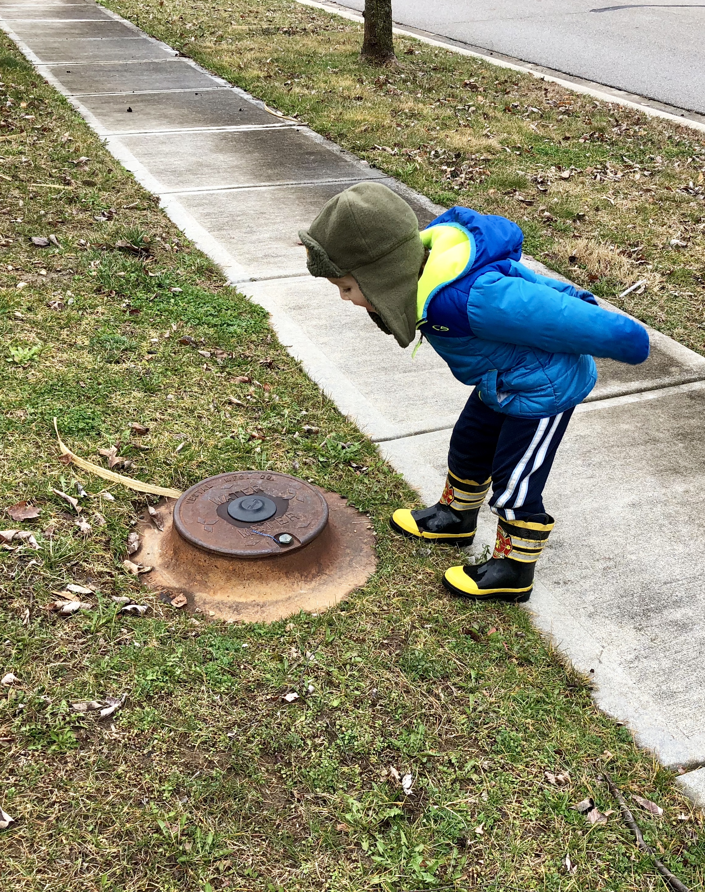 boy leaning over a water access cover and calling out