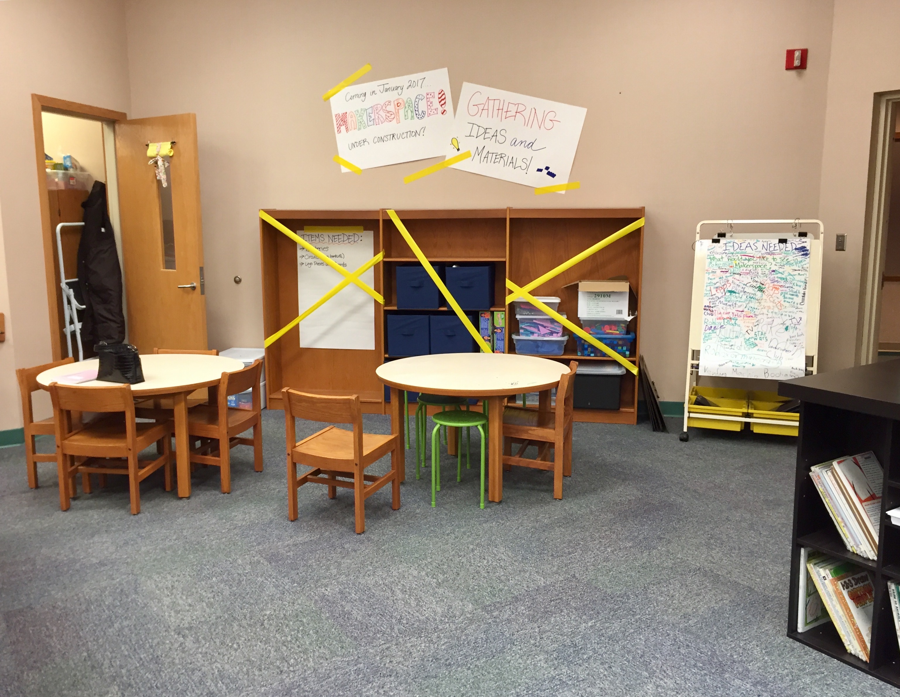 Large empty bookshelf with yellow tape criss crossed over it. @ tables with chairs. Posters on the walls.