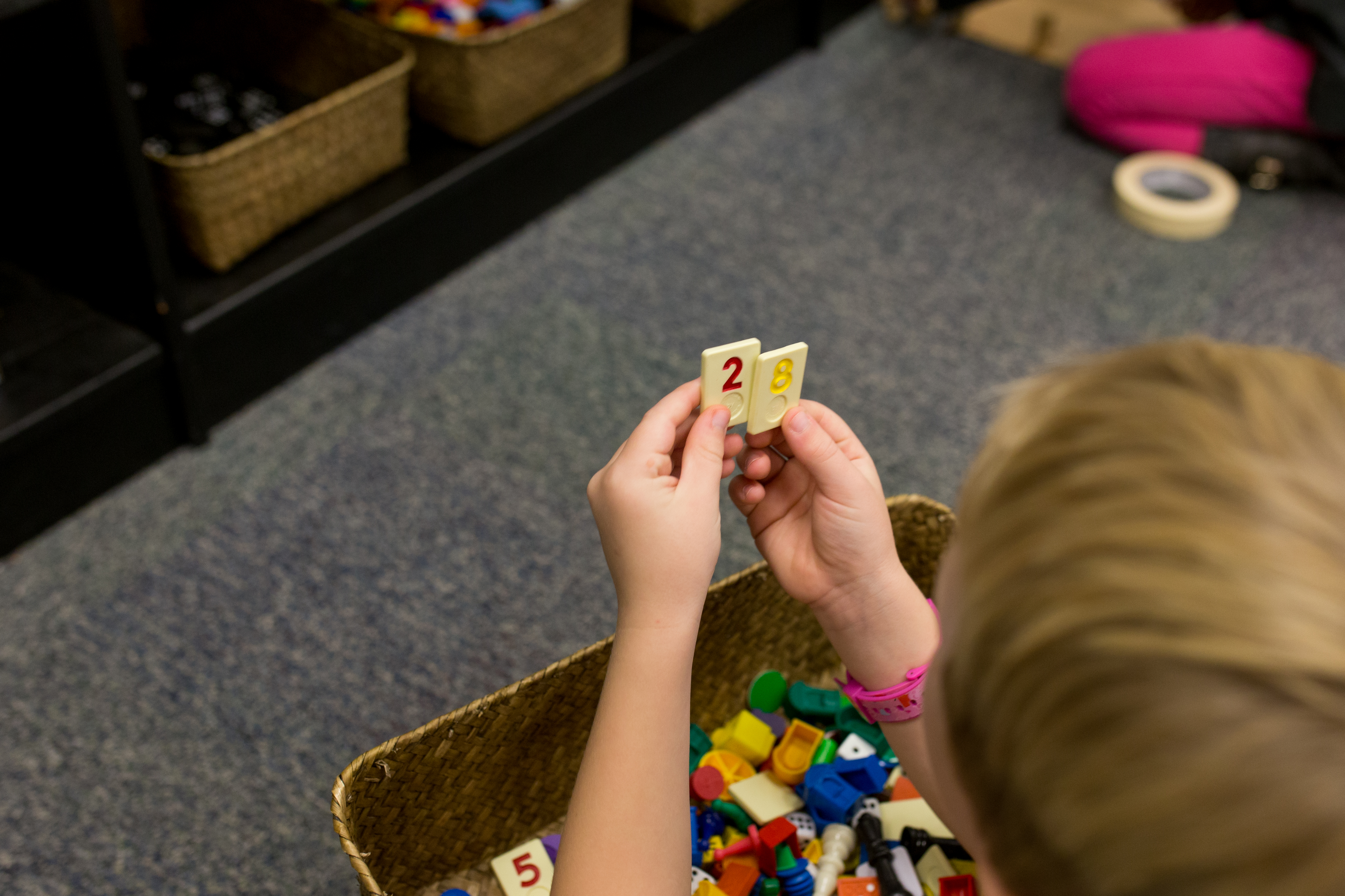 child with a basket of random game pieces and holding up 2 number tiles