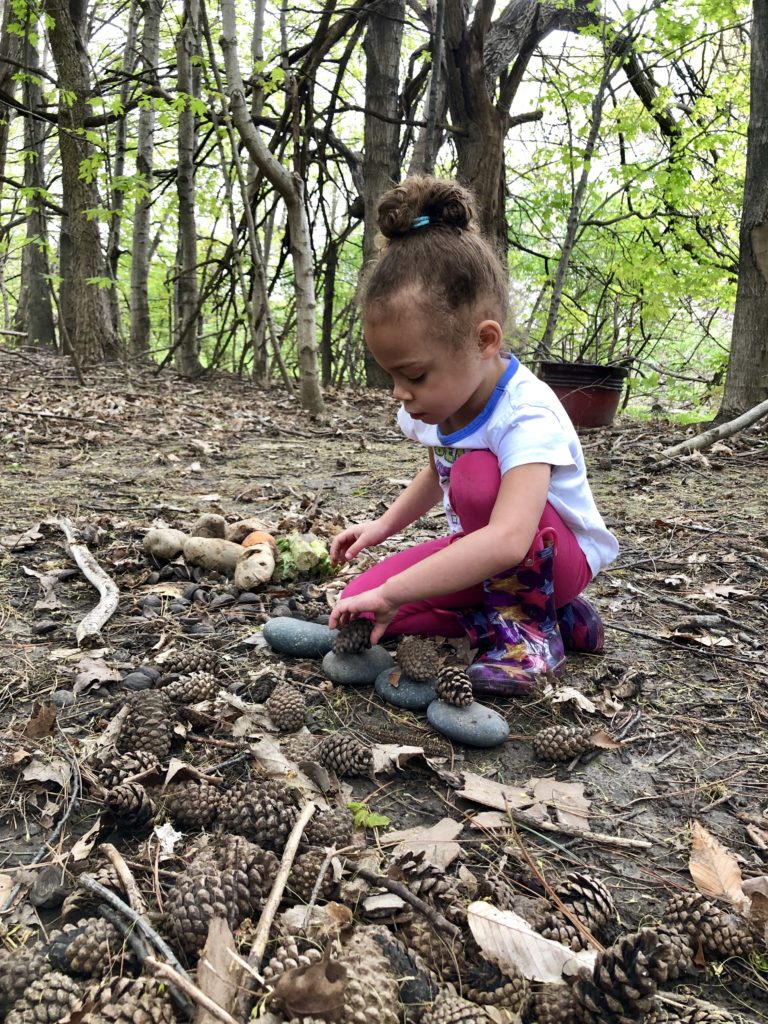 girls stacking pine cones on top of stones