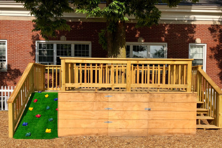 an elevated wood structure with a climbing wall on one side and stairs on the other