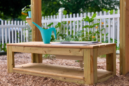 watering pot on a small wooden table with plants growing in the background