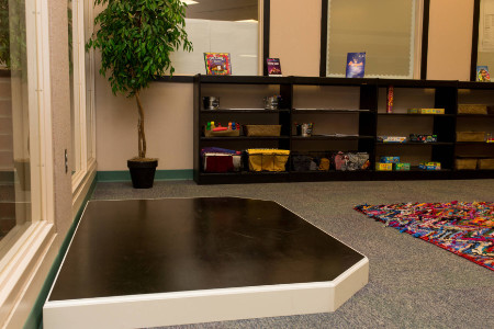 a small stage area on the floor near some book cases holding art supplies