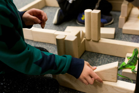 two boys building with wooden blocks. A plastic lizard sits atop one block.