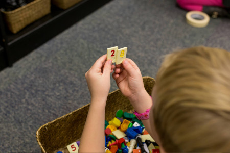 a boy putting numbered tiles next to each other with more numbers in a wicker basket below