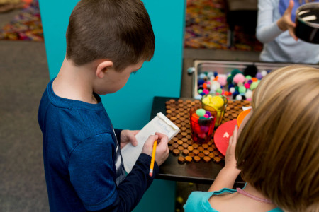 children observing objects on a play kitchen and making sketches and notes in notebooks